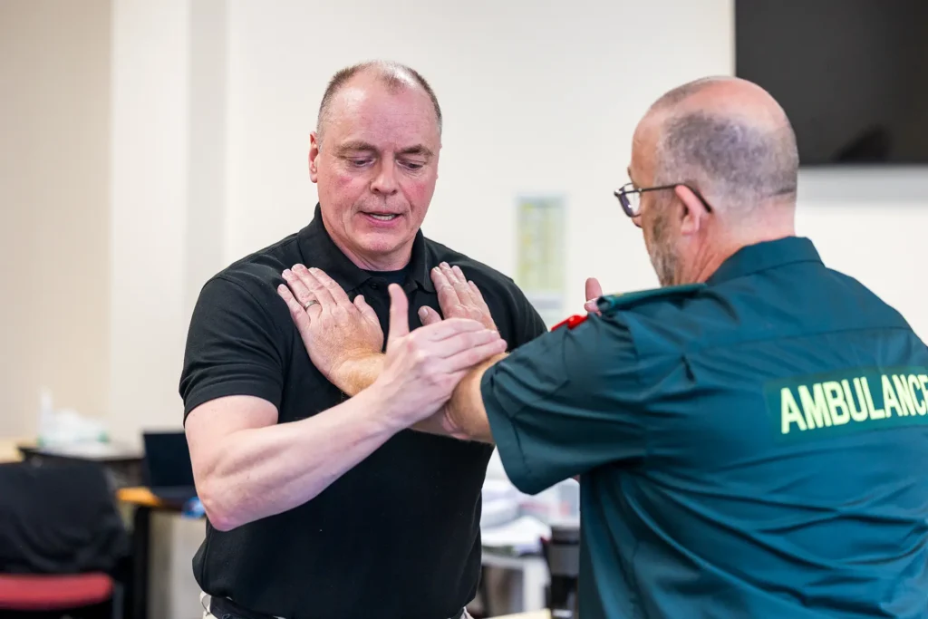 Ambulance worker and a man practicing a physical restraint technique during a training session