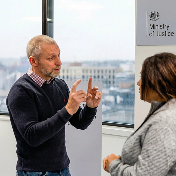 Two people in conversation at a Ministry of Justice office, with a man gesturing expressively while speaking to a woman
