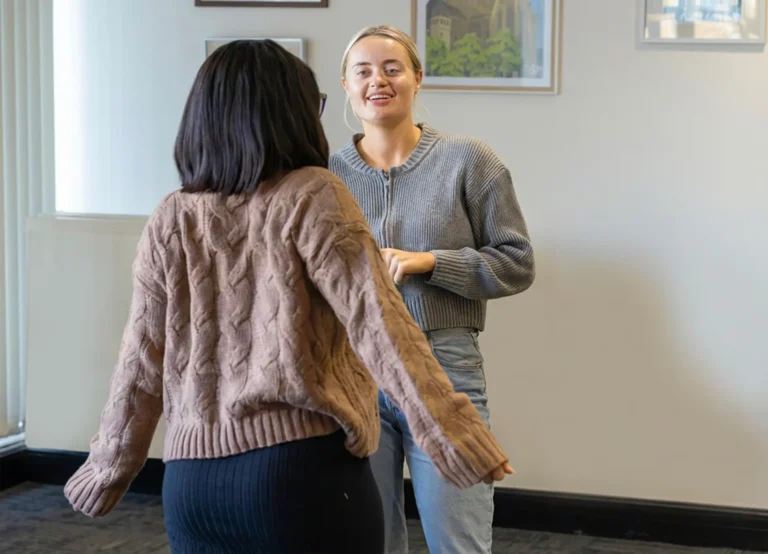 Two women having a friendly conversation in an office, one smiling warmly at the other