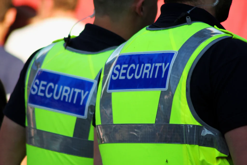 Back view of two security guards wearing high-visibility yellow vests with SECURITY printed on them