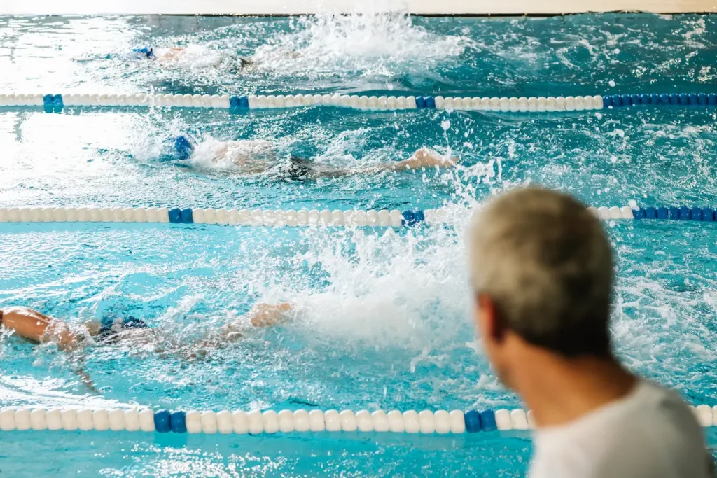 Swimmers in pool lanes with a coach watching from the side
