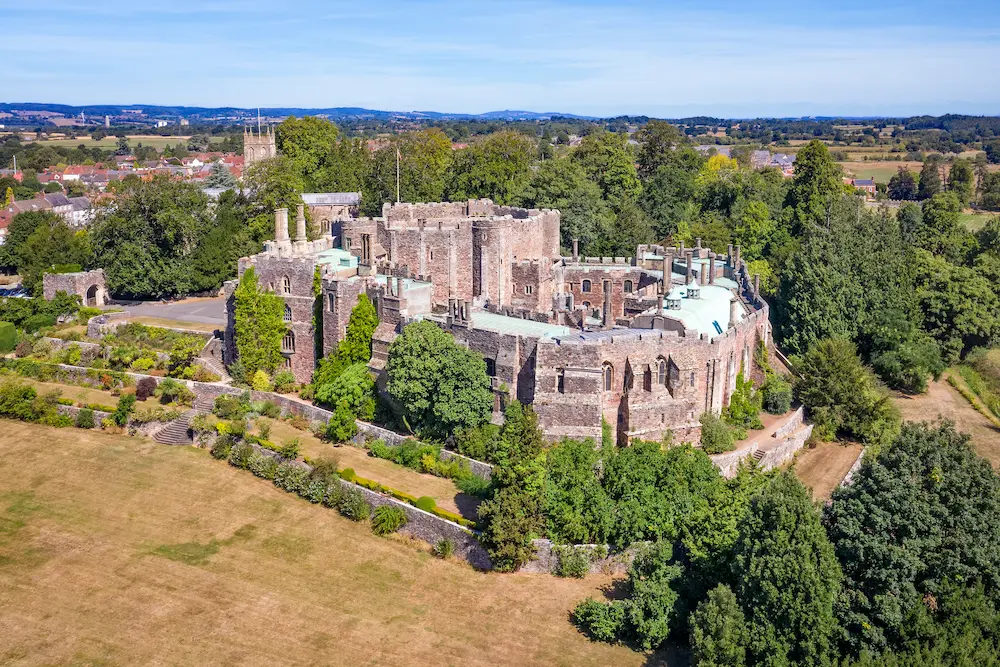 Aerial view of Berkeley Castle, a large stone fortress surrounded by green trees and fields