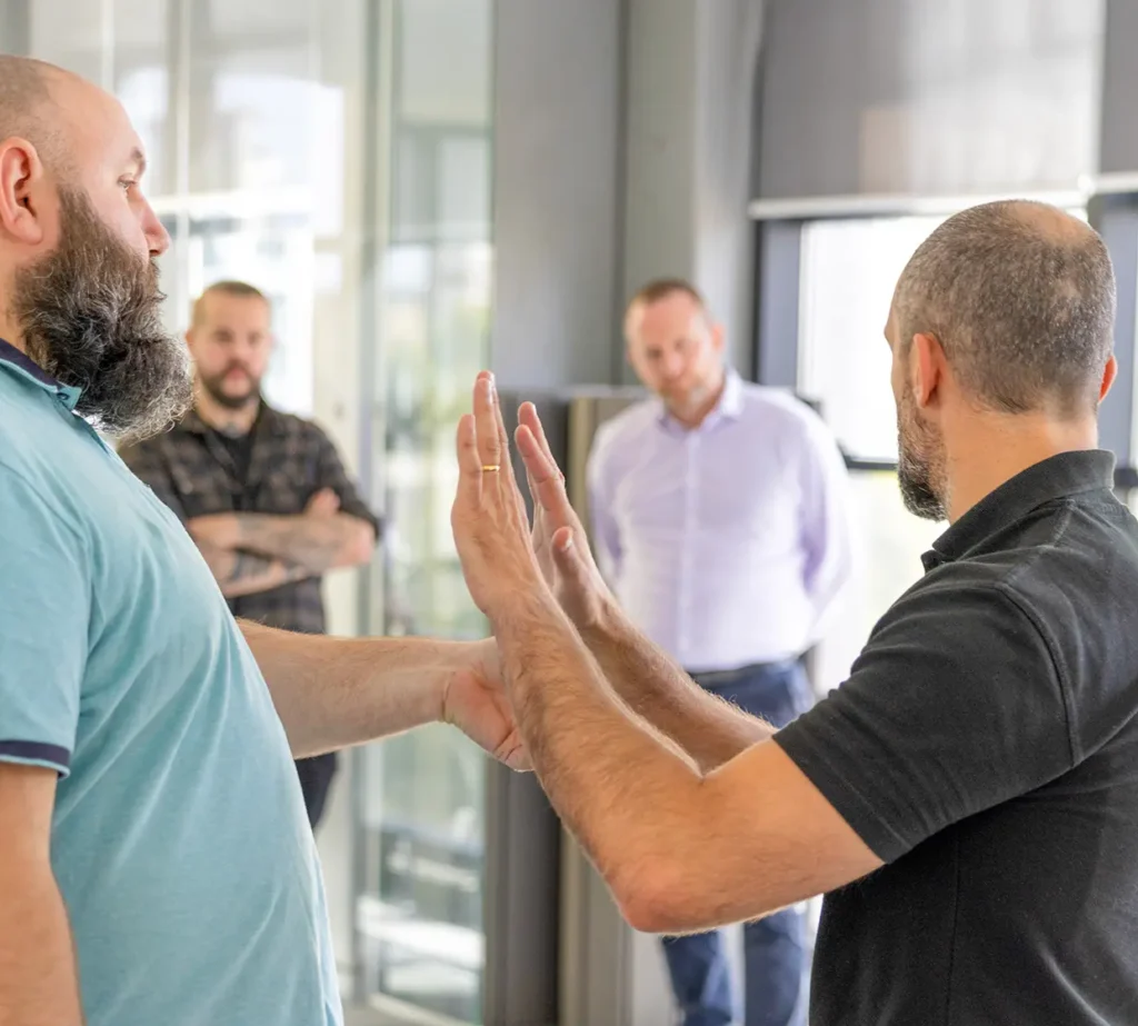 Two men engaged in an animated discussion with hand gestures in an office setting, while two colleagues look on in the background