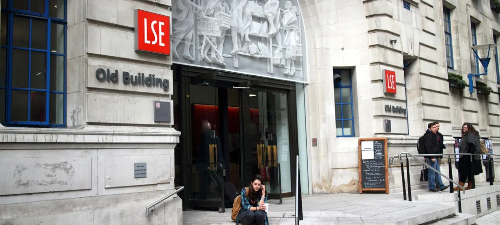 Exterior of the LSE Old Building with students on the steps and a decorative relief sculpture above the entrance