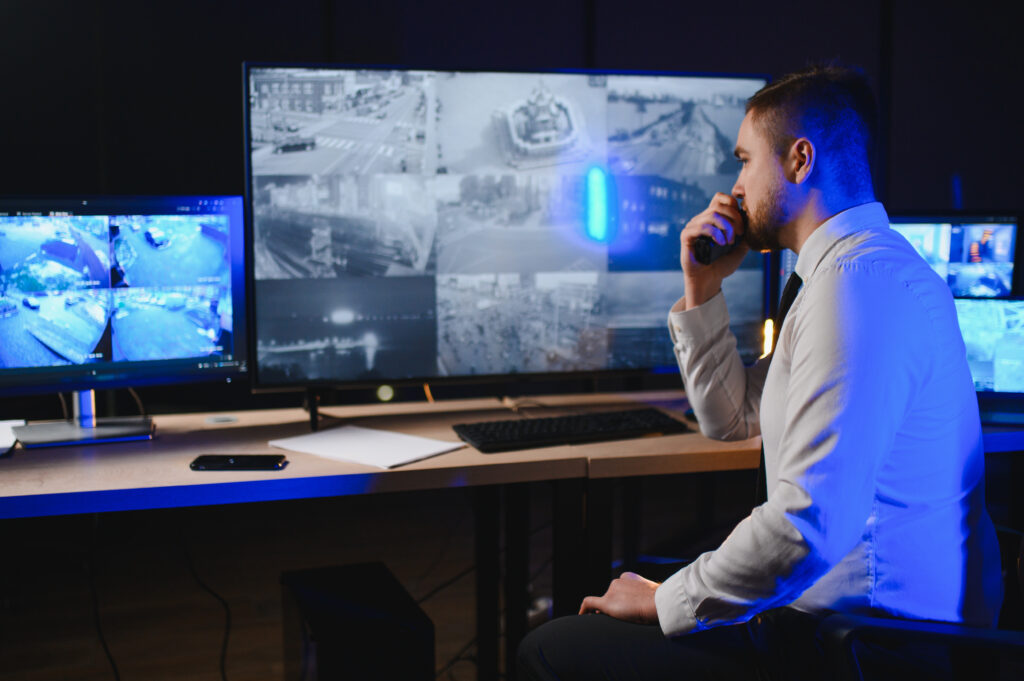 Security guard working late, actively monitoring multiple camera feeds on large screens in a dark control room