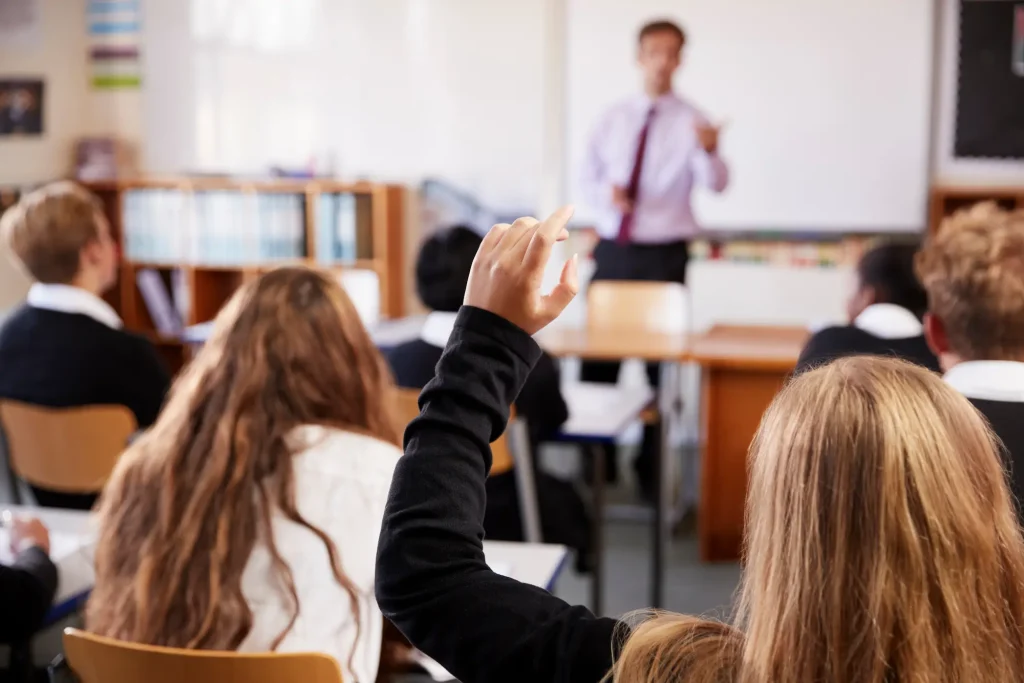 A female student raises her hand to ask a question in a classroom