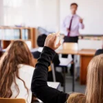 A female student raises her hand to ask a question in a classroom